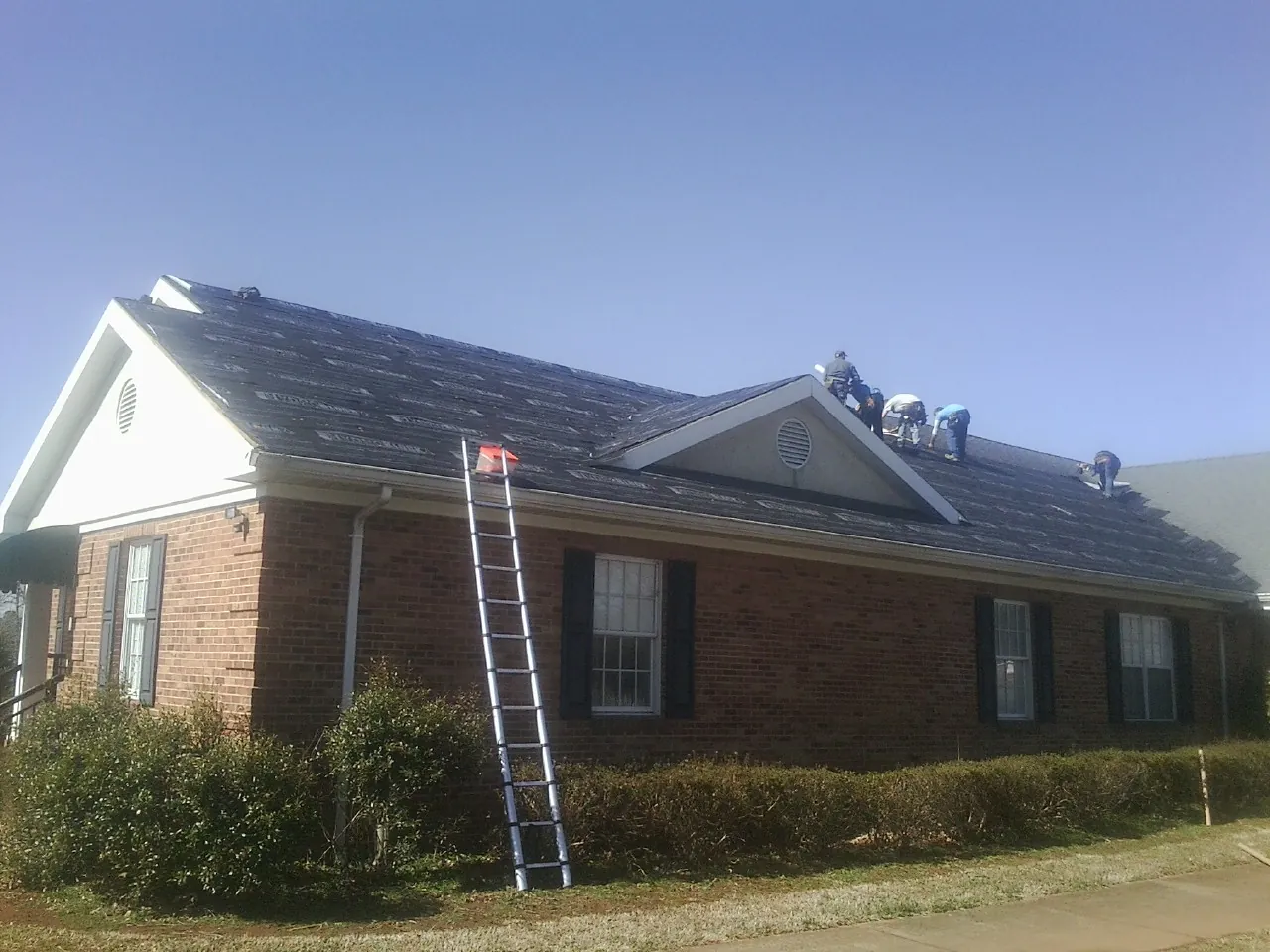 Crew tearing shingles off a brick ranch roof with a ladder set — Emergency Roof Repair work by our crew in Windsor Locks