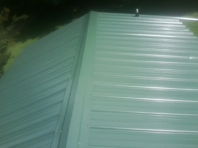 New green metal panels meeting at the ridge of a roof — Flat Roof Repair work by our crew in Windsor Locks